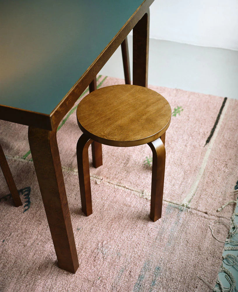 Detaljbilde fra spisestue av mørkebrunt spisebord på rosa teppe med den stablebare krakken Stool E60 i valnøtt fra Artek.
