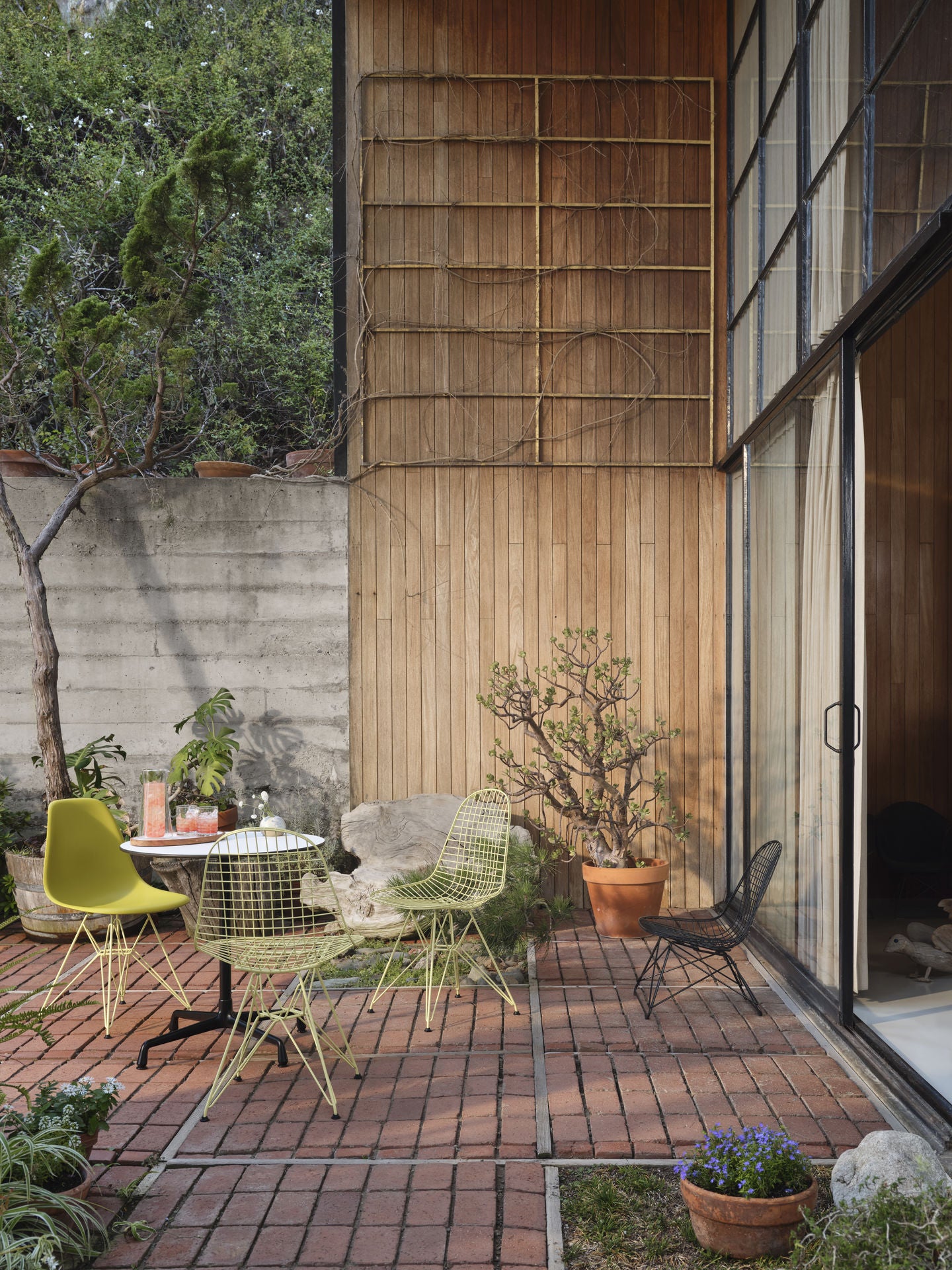 Bilde av Eames Side Chair DSR og Wire Chair DKR i sitrongul farge. Stolene står utendørs på en treplatting inntil et lite kafebord.