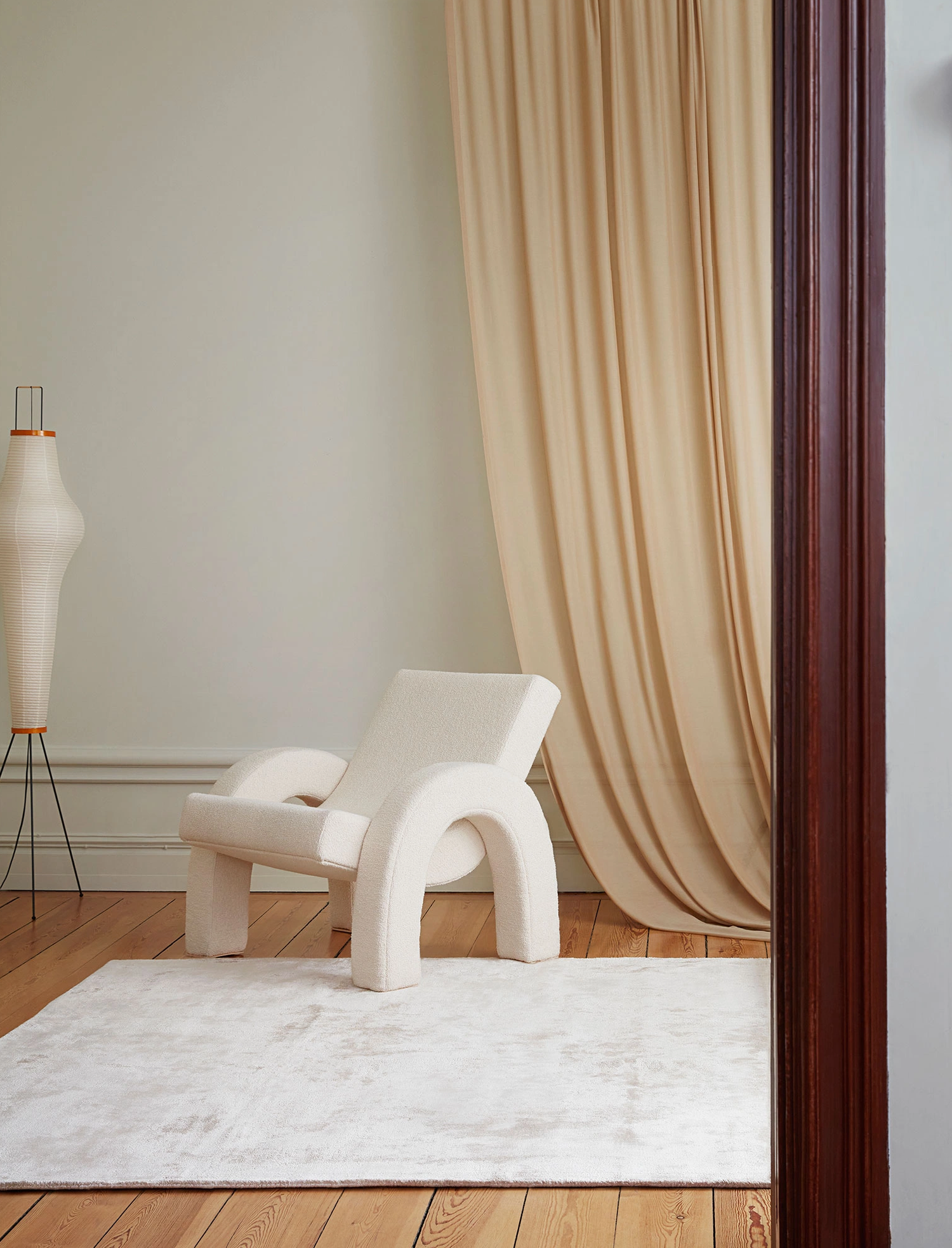 Bilde av den skulpturelle lenestolen Arco fra Dusty Deco i hvit, strukturert boucle stående i vakker stue med tregulv i eik.