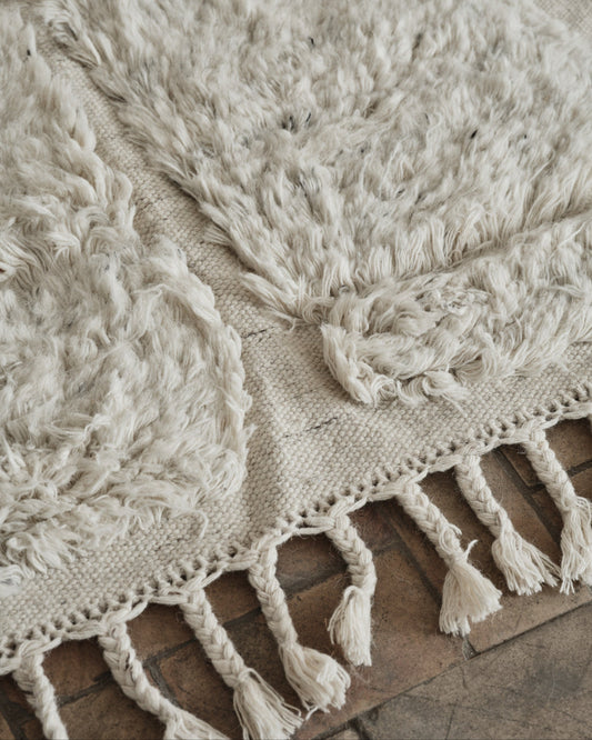 Laget i fargen «shell», en myk, off-white farge, og designet med flettede, tykke frynser på endene er dette et vakkert og lyst – og litt spennende – teppe som vil tilføre ethvert rom et levende uttrykk, enten du har en minimalistisk eller mer maksimalistisk interiørstil.