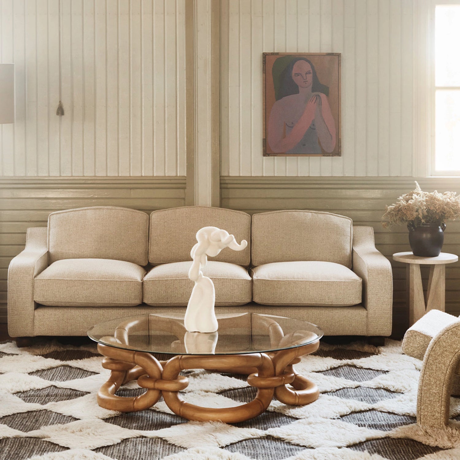 Bilde av den beige sofaen Lola i fargen Sand fra Dusty Deco stående i stue med mønstret teppe og sofabord i tre og glass. 