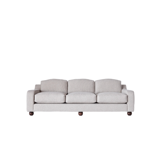 Sofaen Lola i et sandfarget, jaquardvevd møbelstoff. De runde bena er laget av massiv, beiset bøk. Det mørke treverket står i superfin kontrast til det lyse tekstilet.