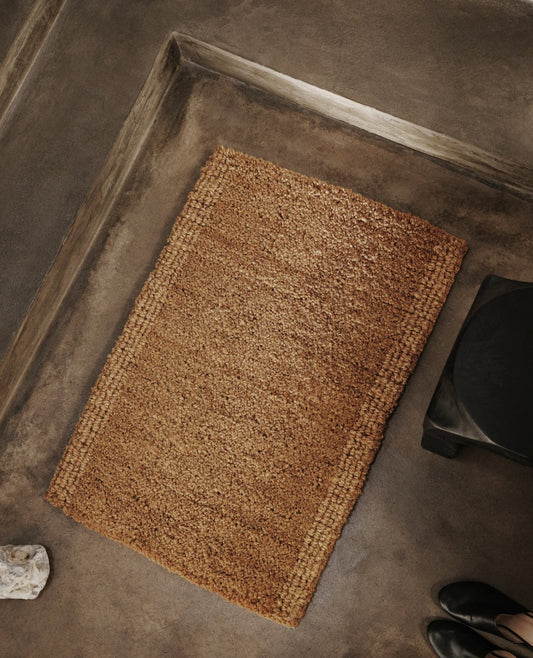 Coir Mat fra Ferm Living er en fin og bærekraftig vevd dørmatte laget av kokosnøttfiber. Disse fibrene sankes fra kokosnøttskallet og hylles spesielt for sin gode holdbarhet og evne til å trekke til seg fuktighet. Matten har to ulike vevde teksturer med en løkket kant i designen, noe som gir den en akkurat passe rustikk touch.