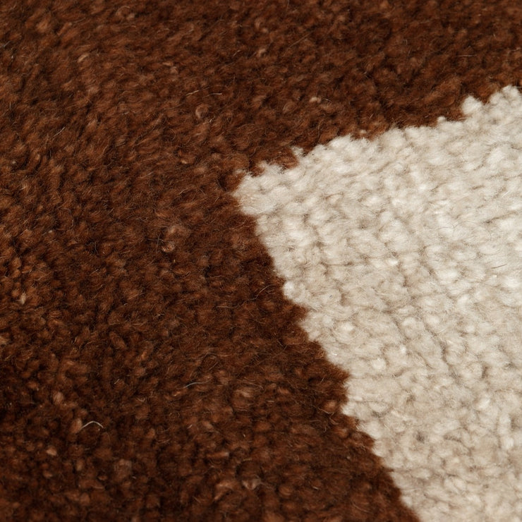 Teppet er rutemønstret i en kombinasjon av mursteinsbrunt og off-white.