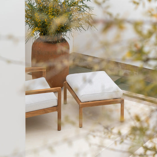 Puffen Jack Outdoor Footstool fra Ethnicraft har en ramme i solid teak som eldes vakkert med tiden, og leveres med en tykk pute i et slitesterkt og værbestandig tekstil – laget for å stå ute hele sommersesongen.