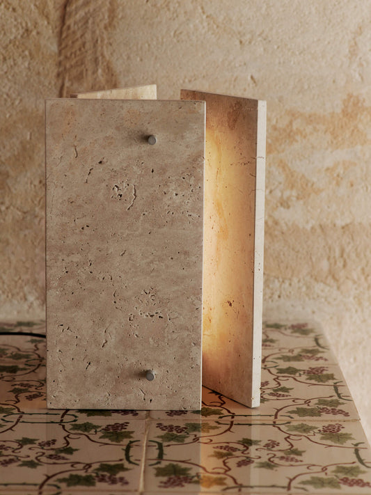 Det stramme designet til bordlampen Oeste Table Lamp fra Ferm Living står i fin kontrast til travertinens naturlige, uregelmessige tekstur, og den varme, sandfargede kalksteinen lar seg lett kombinere med andre materialer og farger i interiøret.