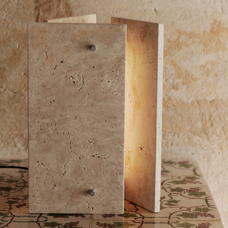 Det stramme designet til bordlampen Oeste Table Lamp fra Ferm Living står i fin kontrast til travertinens naturlige, uregelmessige tekstur, og den varme, sandfargede kalksteinen lar seg lett kombinere med andre materialer og farger i interiøret.
