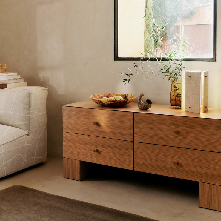 Bordlampen Oeste Table Lamp fra Ferm Living har en elegant visuell tyngde, og består av tre travertinpaneler med en lyskilde som skaper et dynamisk spill mellom lys og skygge.