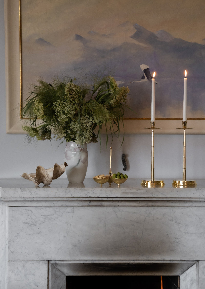 Graceful Candlestick fra Skultuna i forgylt messing brukt som dekorasjon på en peishylle i marmor, med tente lys