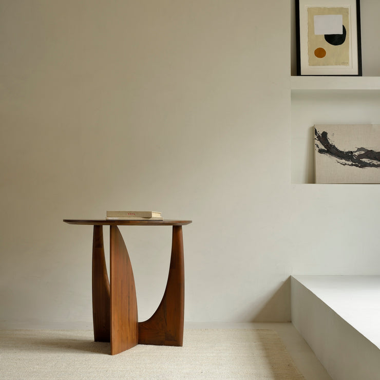 Sidebordet Geometric Side Table fra Ethnicraft er et vakkert og skulpturelt sidebord i heltre med mykt avrundede kanter og et formmessig spennende understell. Buede former og rette vinkler skaper lekne kontraster med lys og skygge og gjør sidebordet til et blikkfang fra alle vinkler.
