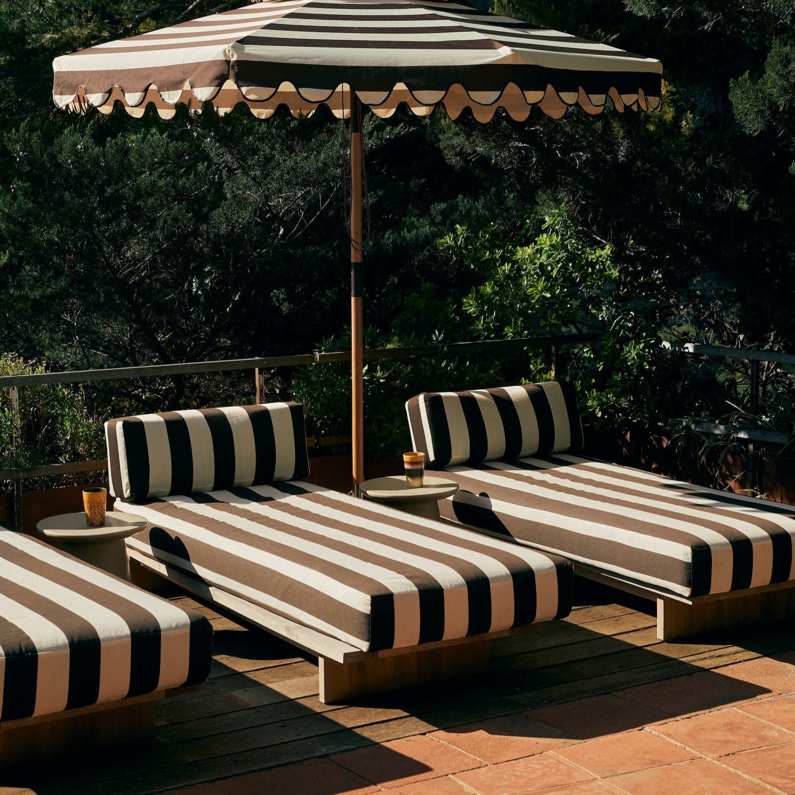 Det mørkebrune- og hvitstripete tekstilet Stracciatella, minner eksempelvis om poolside-møblene i fotografiene til Slim Aarons fra 70-tallet. Så fint! Det finnes også en matchende parasoll. samt at utesofaen i samme serie kan kles i samme tekstil som dagsengen. 