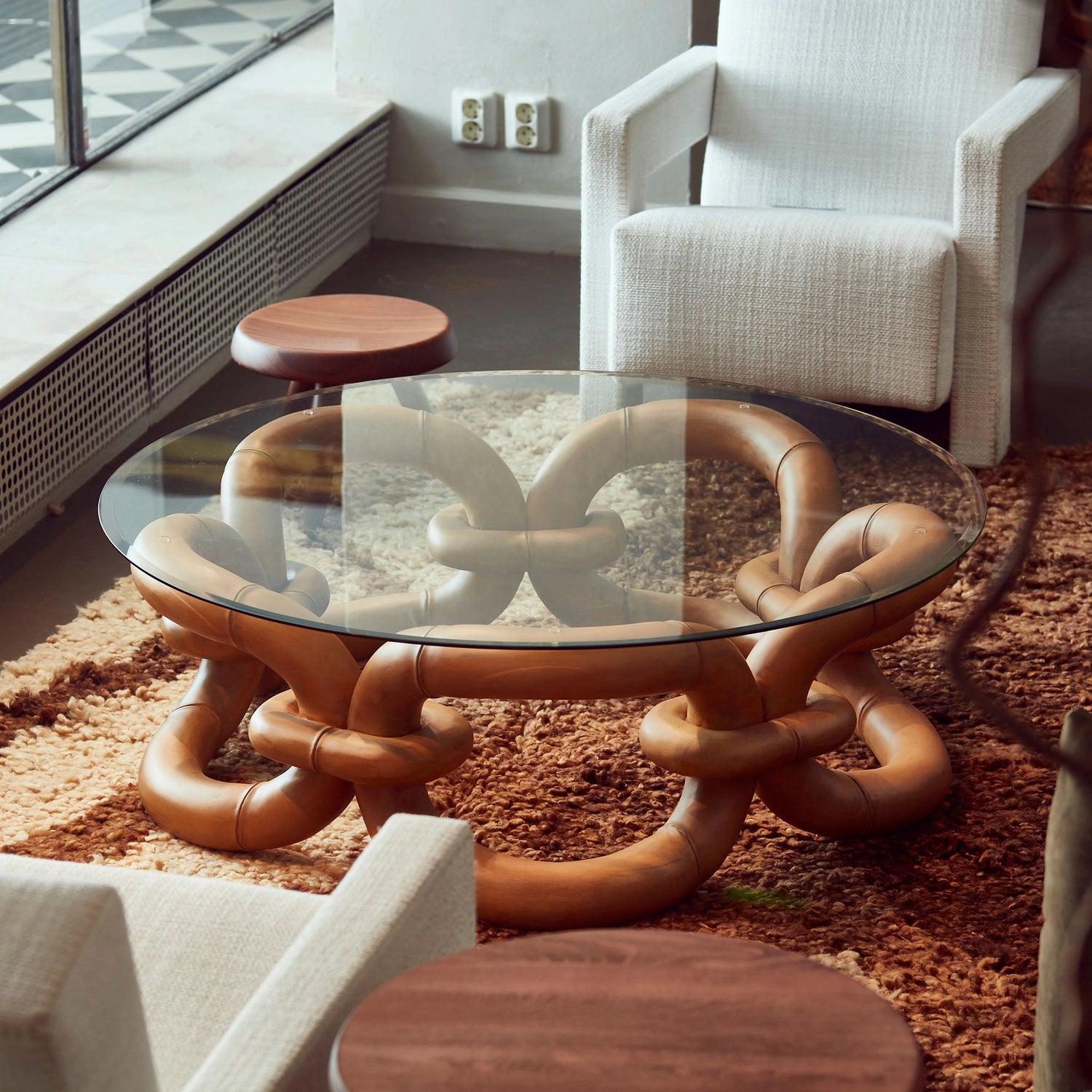 Nærbilde av sofabordet Bamboo Bracelet i tre med glassplate fra Dusty Deco stående på brunt teppe med hvite lenestoler til.