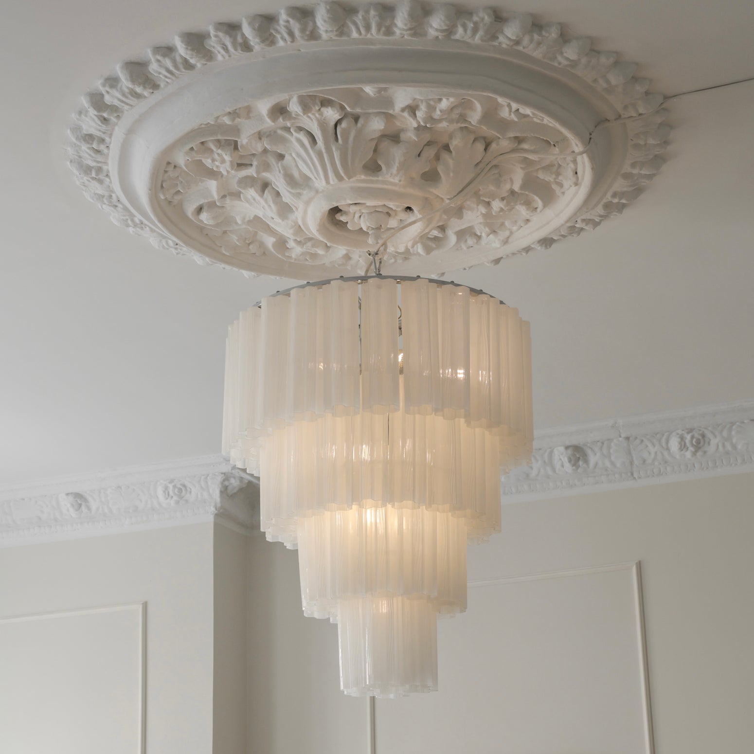 Her ser du lysekronen Fontaine Chandelier 4-layer fra Meublé i hvitt glass og krombelagt oppheng. Den stemningsfulle lysekronen er en del av en serie med lysekroner der du kan velge mellom tre ulike størrelser, der dette er den som bygger mest i høyden. Lysekronen måler Ø65 x H77 cm.