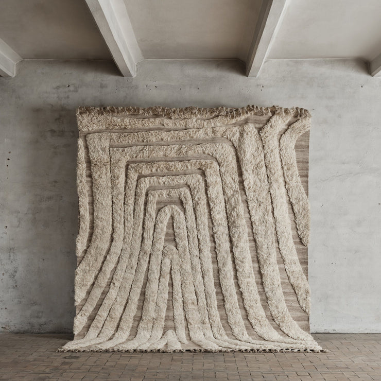 Det myke, uregelmessige mønsteret med lav og høy luvlengde skaper et levende og spennende uttrykk, mens de vakre frynsene tilfører en kunstnerisk detalj.