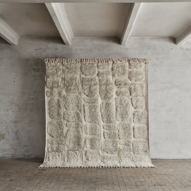 Teppet er håndvevd og laget i naturlig, ubleket New Zealand-ull og bomull og kommer i to størrelser: 230x280 cm og 290x350 cm.