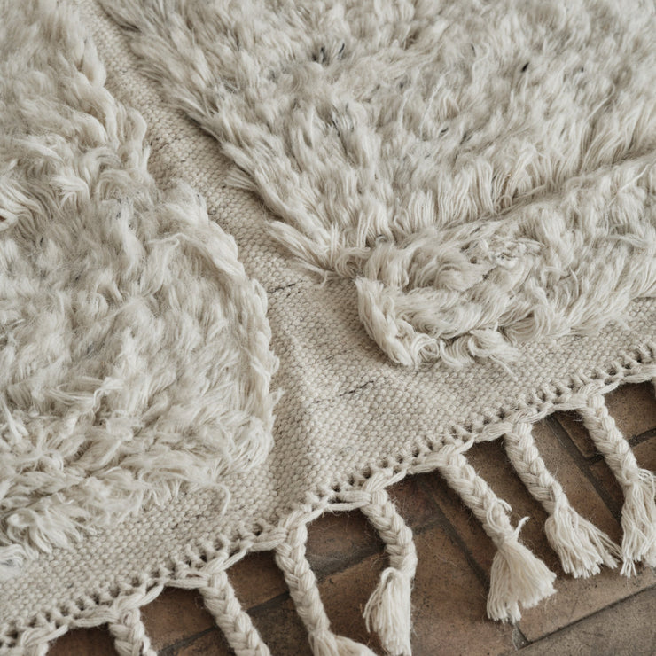Laget i fargen «shell», en myk, off-white farge, og designet med flettede, tykke frynser på endene er dette et vakkert og lyst – og litt spennende – teppe som vil tilføre ethvert rom et levende uttrykk, enten du har en minimalistisk eller mer maksimalistisk interiørstil.