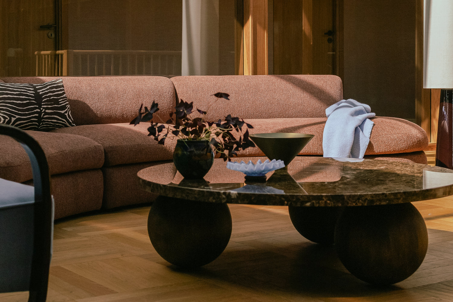 Buet sofa Coda fra New Works i rustfarget bouclétekstil fra OsloDeco i atriumstue renovert av AlexArk. Stuen har varme finerkledde vegger og vakkert håndplukket interiør i en helhetlig stil. I front står et sofabord med steinplate i brun Emperador-marmor. Detaljer i messing og lys blått. Foto: OsloDeco