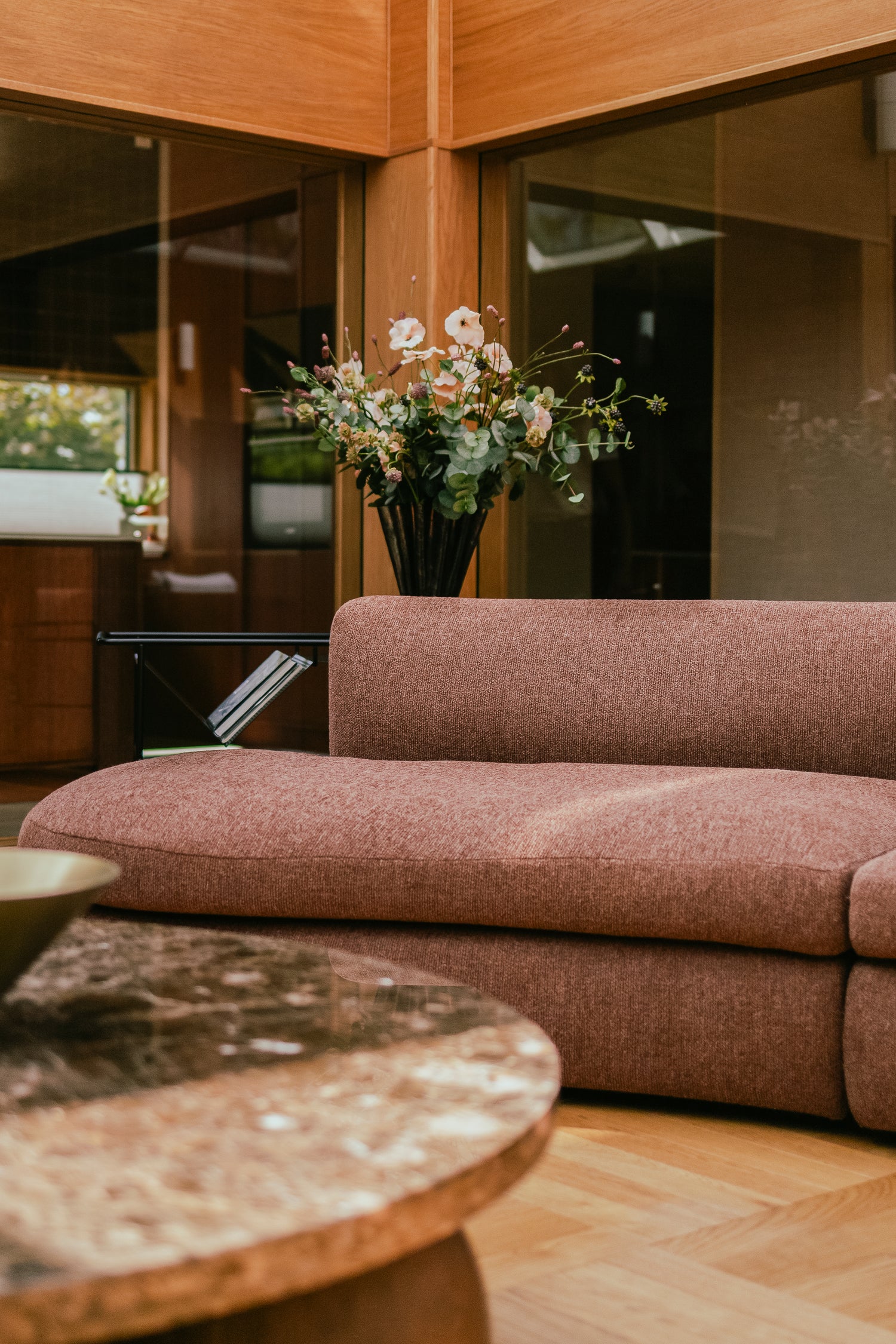 Buet sofa Coda fra New Works i rustfarget bouclétekstil fra OsloDeco i atriumstue renovert av AlexArk. Stuen har varme finerkledde vegger og vakkert håndplukket interiør i en helhetlig stil. Foto: OsloDeco