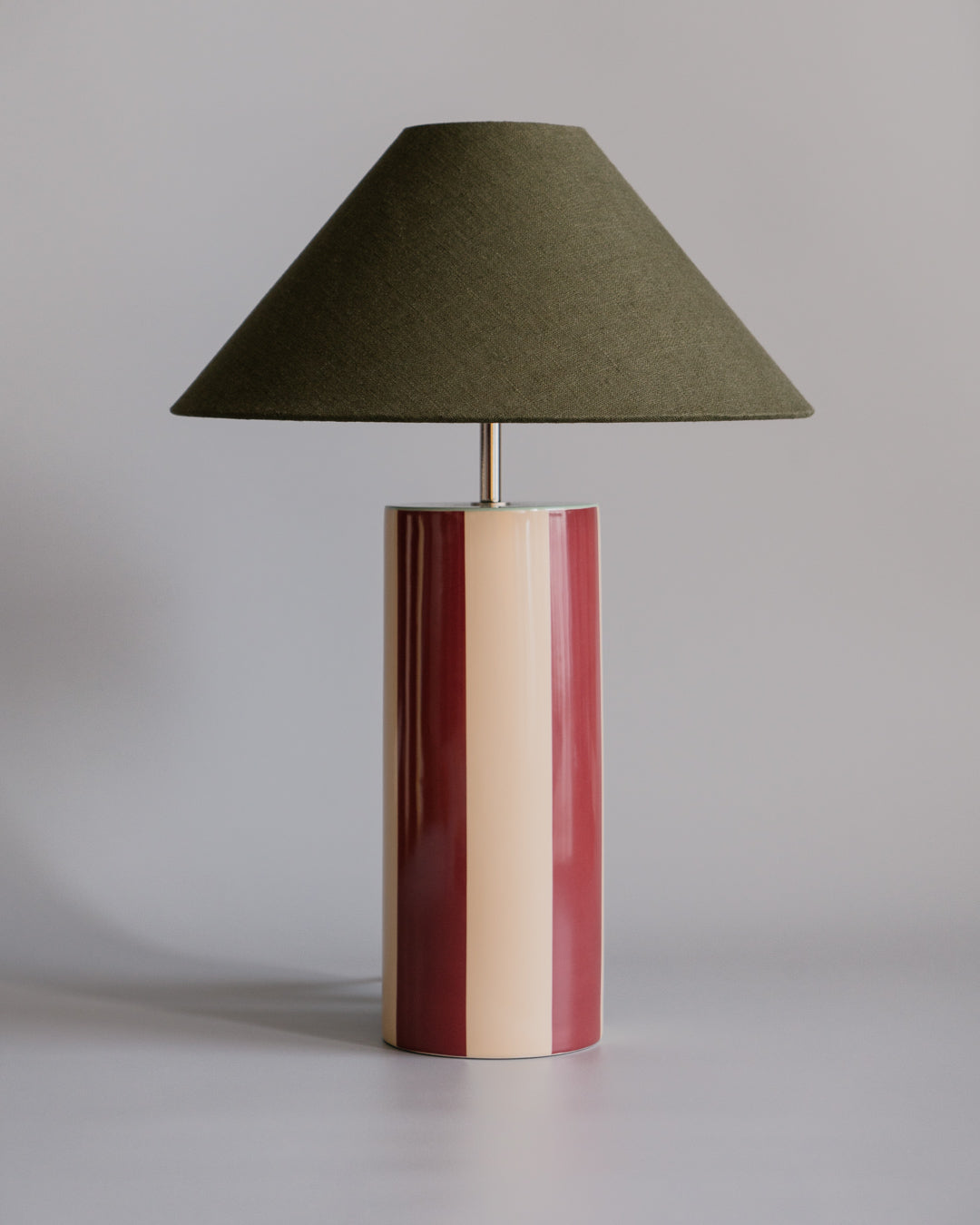 Bordlampen Ombrellina Oxblood & Seaweed, i høyblank glasert okseblodrød- og smørkremgulglasert stripete keramikk med mintfarget topp, tilhører Renaissance-kolleksjonen, som er inspirert av fargene brukt av malemestere under renessansen samt interiøret fra denne tidsepoken, da mørkt treverk og dype, varme farger regjerte. Formen er likevel moderne – og vi elsker uttrykket!