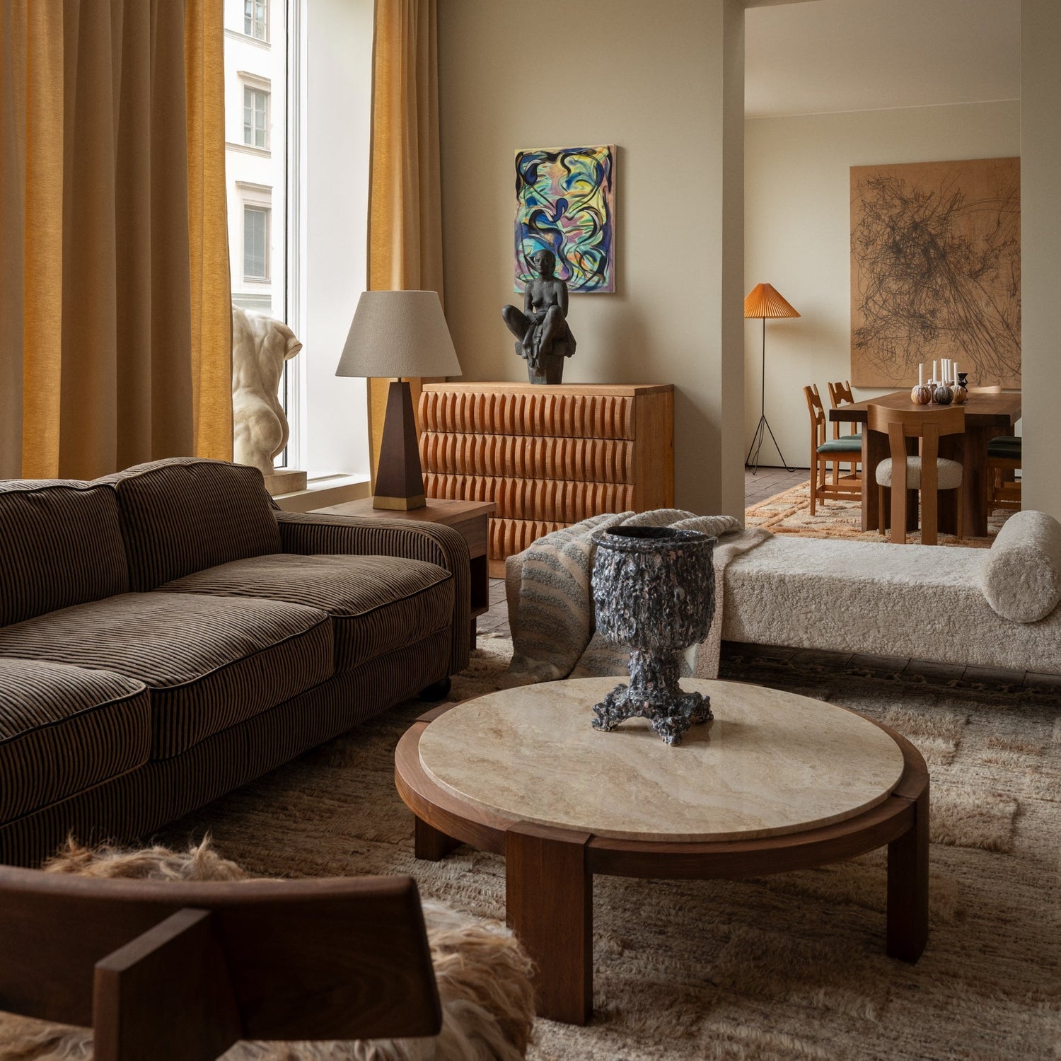 Det runde sofabordet Dean Coffee Table fra Dusty Deco med ramme i oljet valnøtt og bordplate i travertinstein tilfører stuen din et vakkert tyngdepunkt. Kontrasten mellom det varme treverket og den kjøligere steinen skaper et balansert uttrykk som føles både moderne og tidløst.