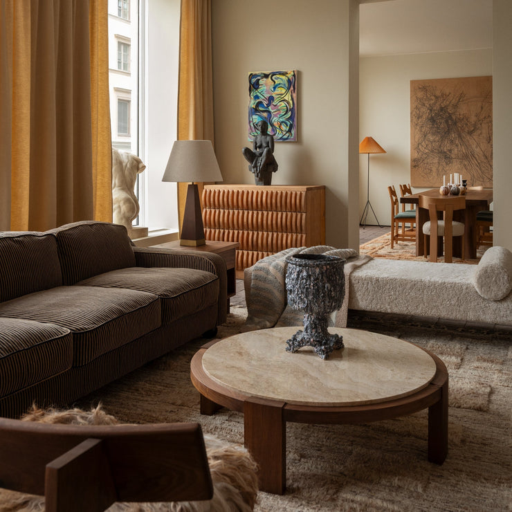 Det runde sofabordet Dean Coffee Table fra Dusty Deco med ramme i oljet valnøtt og bordplate i travertinstein tilfører stuen din et vakkert tyngdepunkt. Kontrasten mellom det varme treverket og den kjøligere steinen skaper et balansert uttrykk som føles både moderne og tidløst.