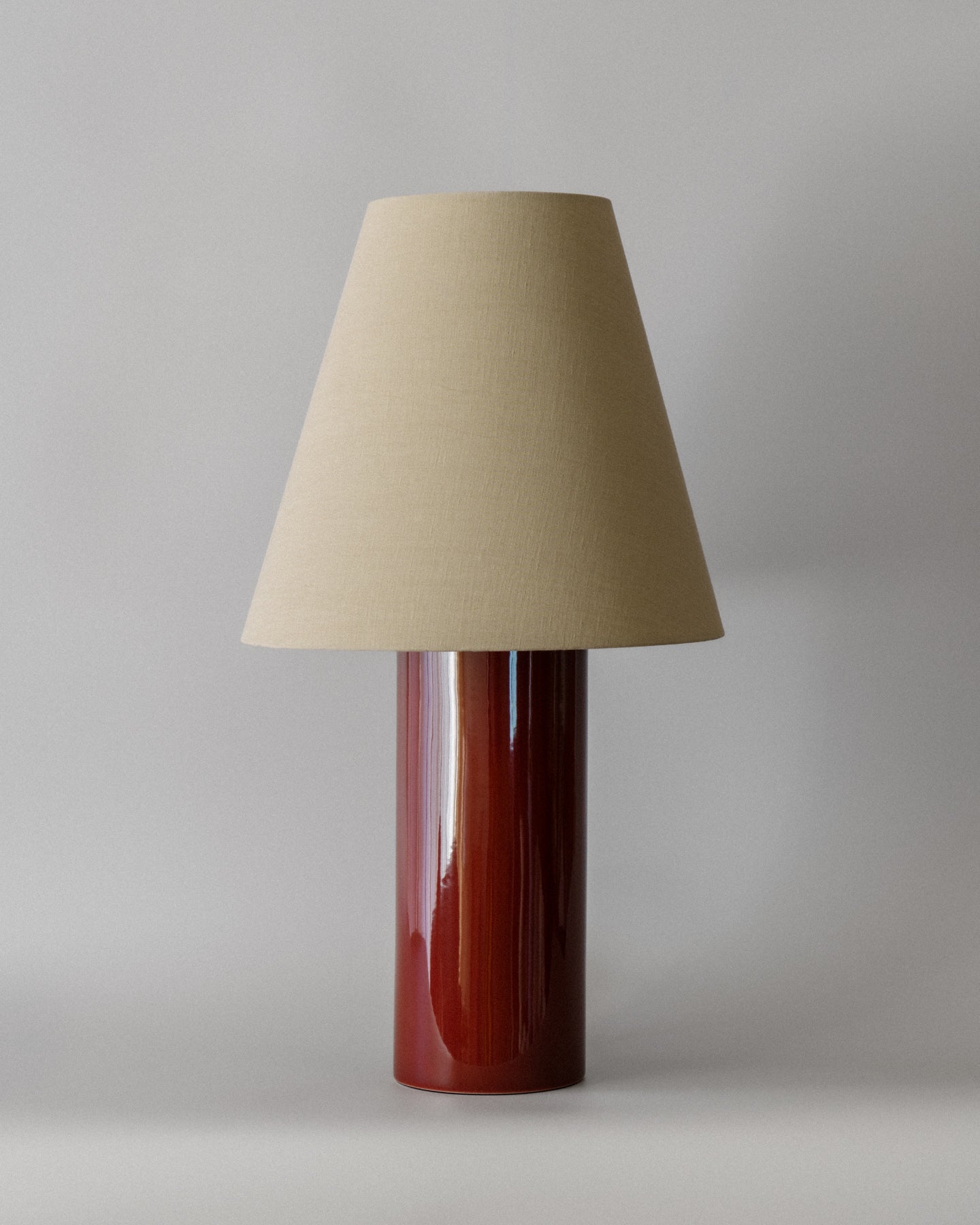 Bordlampen Giro Oxblood & Beige har en keramisk sylinderformet lampefot med en dyp okseblodfarget glasur og en konisk skjerm drapert i en teksturert lys beige bomull (fra Haider Ackermann) som sprer et behagelig og stemningsfullt varmt lys. En raffinert bordlampe som vil tilføre ethvert rom en dose sofistikert eleganse!