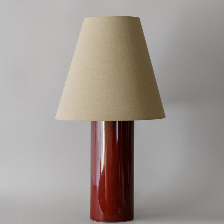 Bordlampen Giro Oxblood & Beige har en keramisk sylinderformet lampefot med en dyp okseblodfarget glasur og en konisk skjerm drapert i en teksturert lys beige bomull (fra Haider Ackermann) som sprer et behagelig og stemningsfullt varmt lys. En raffinert bordlampe som vil tilføre ethvert rom en dose sofistikert eleganse!