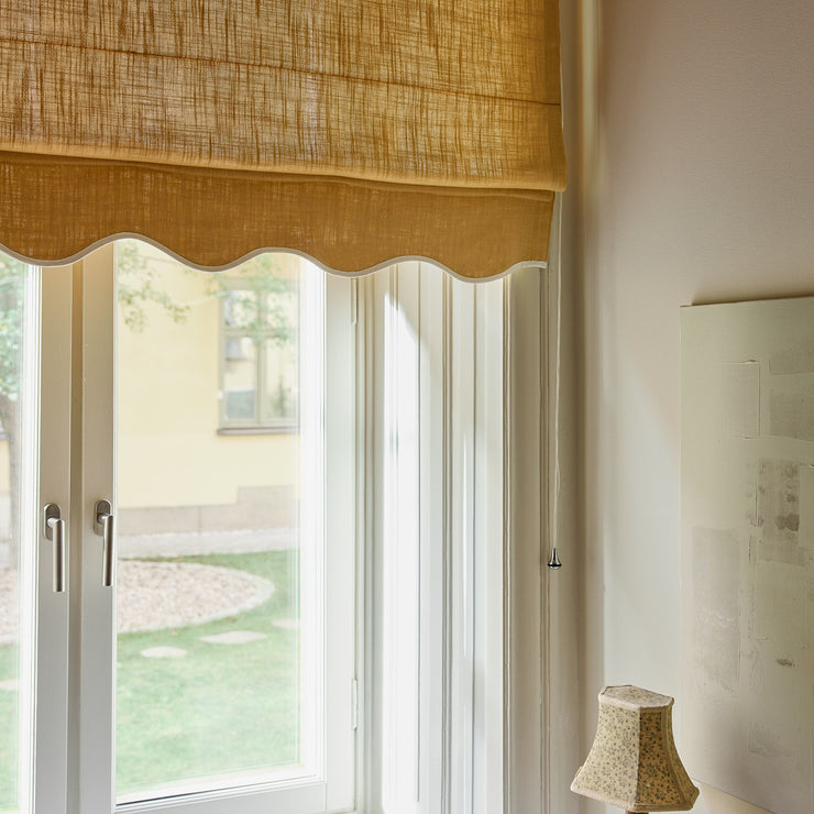 Liftgardin Scallop Edge i vevd lin fra Gotain: Den vakkert bølgede kanten står i nydelig kontrast til hovedfargen. Velg mellom kombinasjonene Sand Mustard, Mustard Sand, Ivory Terracotta og Terracotta Ivory. Alle variantene demper lyset og gir interiøret et lunere preg.