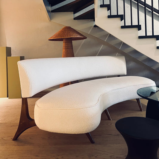Vintagesofaen Floating Curved Sofa ble designet av Vladimir Kagan i 1952, en amerikansk møbeldesigner som hadde tidlig suksess med sine polstrede, organiske former. Vi elsker de myke linjene, det lyse, strukturerte bouclé-tekstilet og de elegante bena i valnøtt.