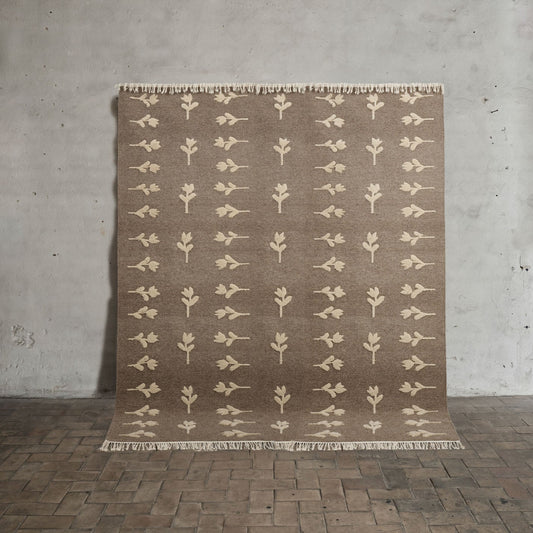 Teppet no.18 fra Cappelen Dimyr er et stort lett, flatvevd teppe i naturlig ull og bomull i en gråbrunfarge med lys beige håndvevde blomster som er inspirert av gamle skandinaviske tulipanmønstre. Det er så vakkert!