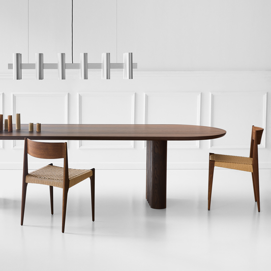 Spisebordet Plush Table fra dk3: Her hviler en oval bordplate på bordben som er satt sammen av en rekke med sylinderformer i tre, som skaper en vakkert bølget effekt på hver ende. Felles for alle spisebord fra dk3 er at designet understreker skjønnheten og de naturlige egenskapene til treet – og Plush Table er intet unntak.