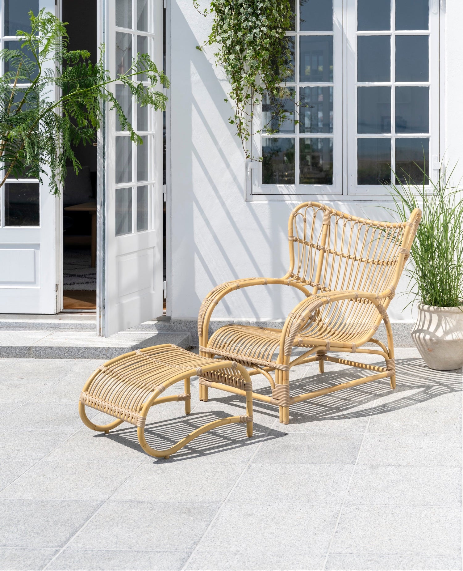 Teddy Lounge Chair og Teddy Footstool fra Sika Design på terrasse utendørs, naturfarget Alu-Rattan