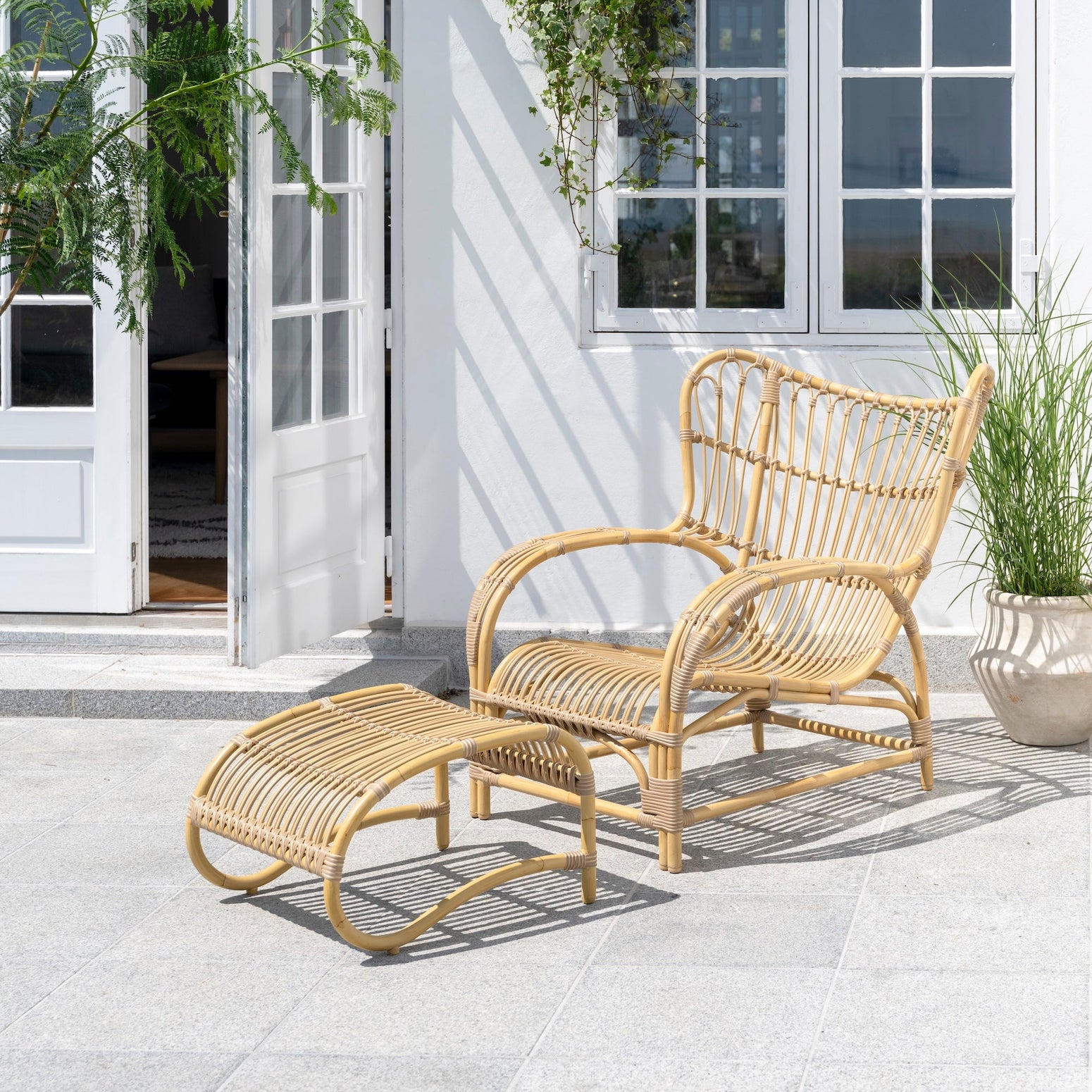 Teddy Lounge Chair og Teddy Footstool fra Sika Design på terrasse utendørs, naturfarget Alu-Rattan