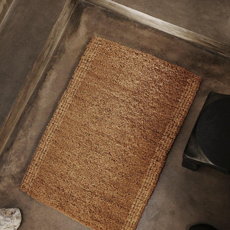 Coir Mat fra Ferm Living er en fin og bærekraftig vevd dørmatte laget av kokosnøttfiber. Disse fibrene sankes fra kokosnøttskallet og hylles spesielt for sin gode holdbarhet og evne til å trekke til seg fuktighet. Matten har to ulike vevde teksturer med en løkket kant i designen, noe som gir den en akkurat passe rustikk touch.