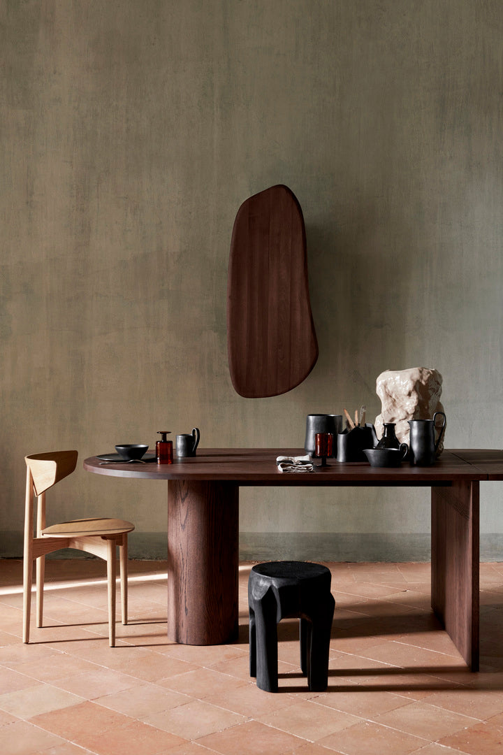 Bilde av spennende interiør med lys trestol, mørkebrunt spisebord, mørkebrunt, vegghengt skap og svart krakk. Alt er fra Ferm Living.