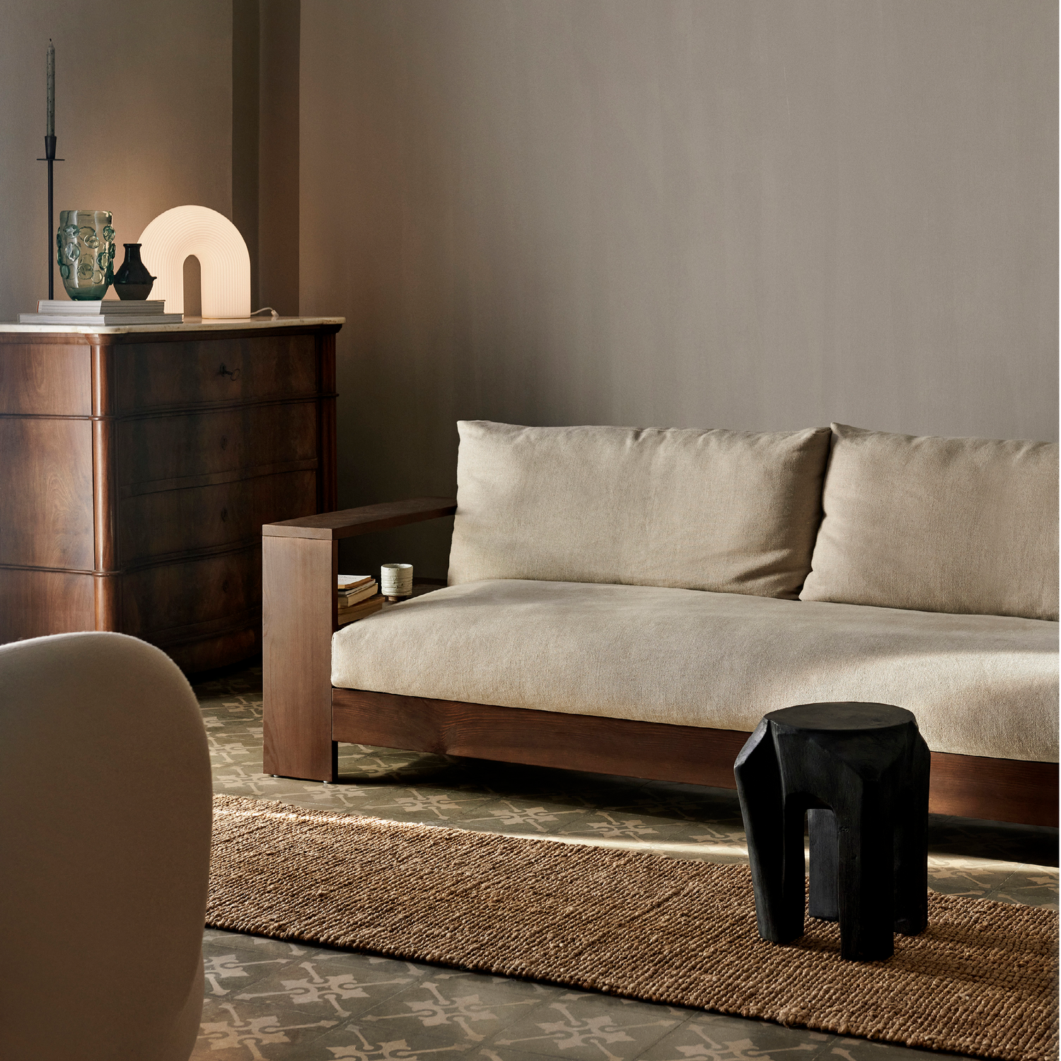 Bilde av stemningsfull stue med møbler i mørkebrunt tre. Sofaen Edre fra Ferm Living har ramme i tre og myke puter i lys lin.