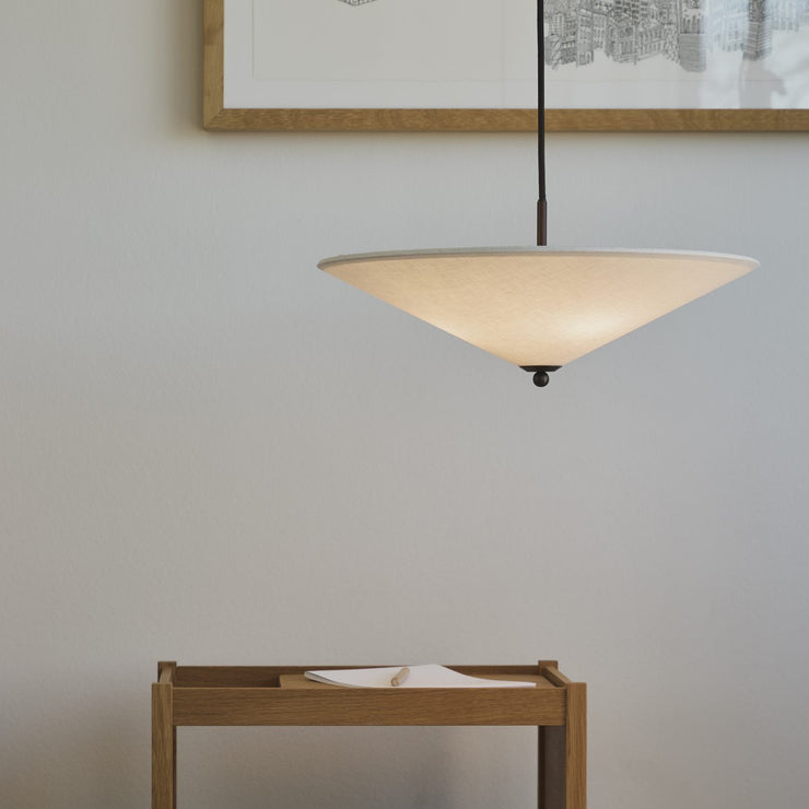 Futé 400 Tipp er en pendellampe fra Lyfa med en rund, konveks skjerm i et kremfarget kanvastekstil med detaljer i brunert messing, designet av det dansk-italienske studioet GamFratesi.
