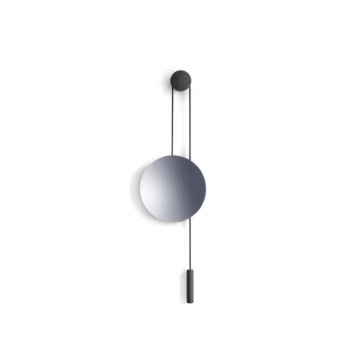 Speilet Rise &amp; Shine fra New Works er et vegghengt speil, som som ser ut som en pendel og har en motvekt i messing.