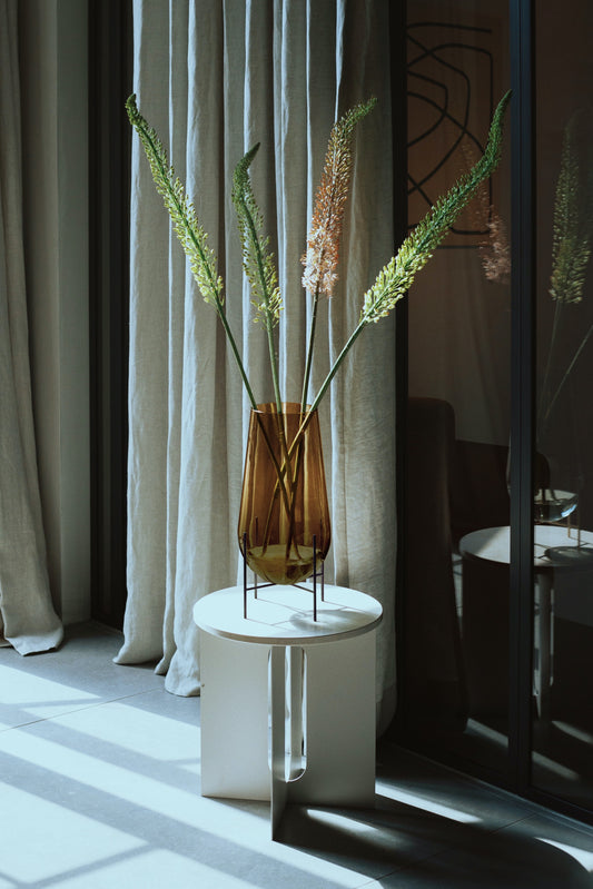 Vaseserien Échasse, designet av Theresa Rand for Menu, har fått et nydelig farge- og materialtilskudd når hun nå har kombinert gyllent, ravfarget glass med slanke ben i brunert messing! Fyll den med grønne vekster, enkle grener eller en frodig og vilter bukett - den dråpeformede vasen står støtt uansett hva du måtte ønske.