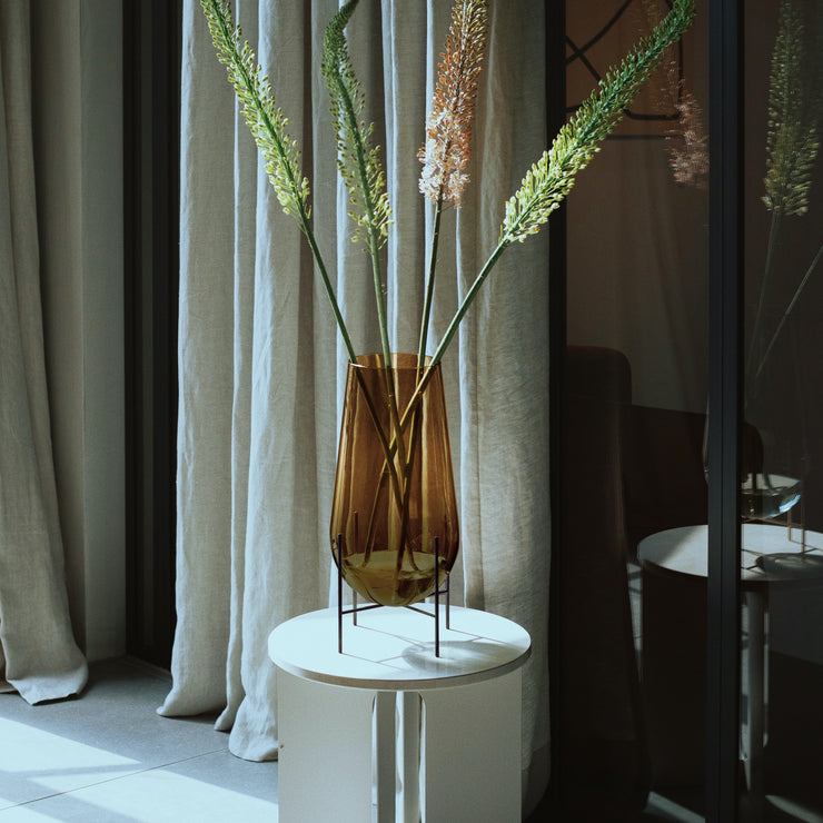 Vaseserien Échasse, designet av Theresa Rand for Menu, har fått et nydelig farge- og materialtilskudd når hun nå har kombinert gyllent, ravfarget glass med slanke ben i brunert messing! Fyll den med grønne vekster, enkle grener eller en frodig og vilter bukett - den dråpeformede vasen står støtt uansett hva du måtte ønske.