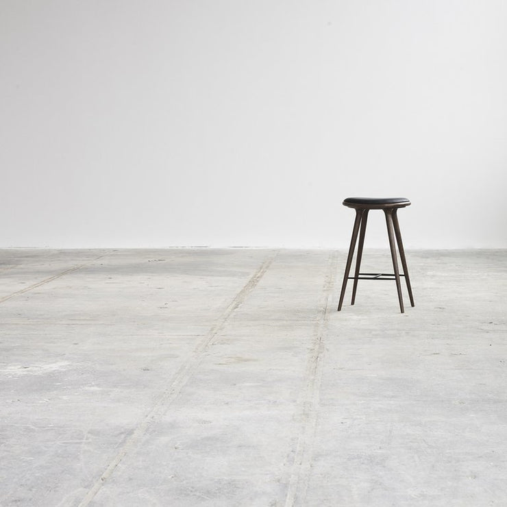 Mater High Stool har et organisk og minimalistisk uttrykk. Eiken er behandlet til en mørk og grålig farge, skinnet på setet er svart. 