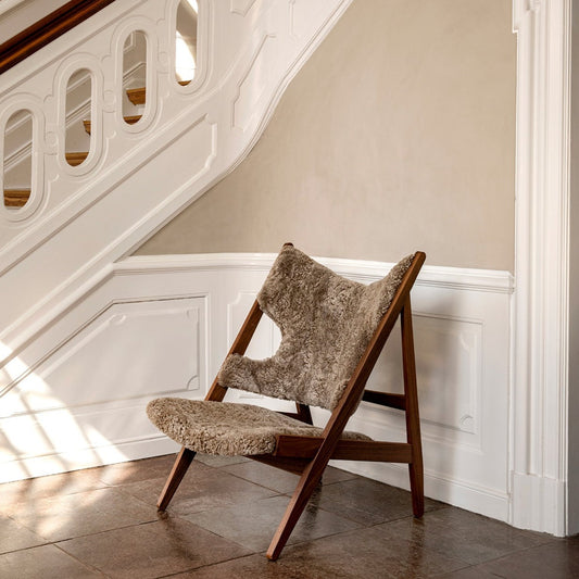 The Knitting Chair ble opprinnelig designet av den danske arkitekten og møbeldesigneren Ib Kofod-Larsen i 1951. Menu har relansert den ikoniske stolen og den finnes nå i ulike varianter, deriblant med base i valnøtt og mykt, deilig saueskinn.