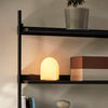 Med en firkantet base og buet topp i farget glass, gjør den geometriske formen at lampen skifter uttrykk avhengig av hvilken side du ser den fra.